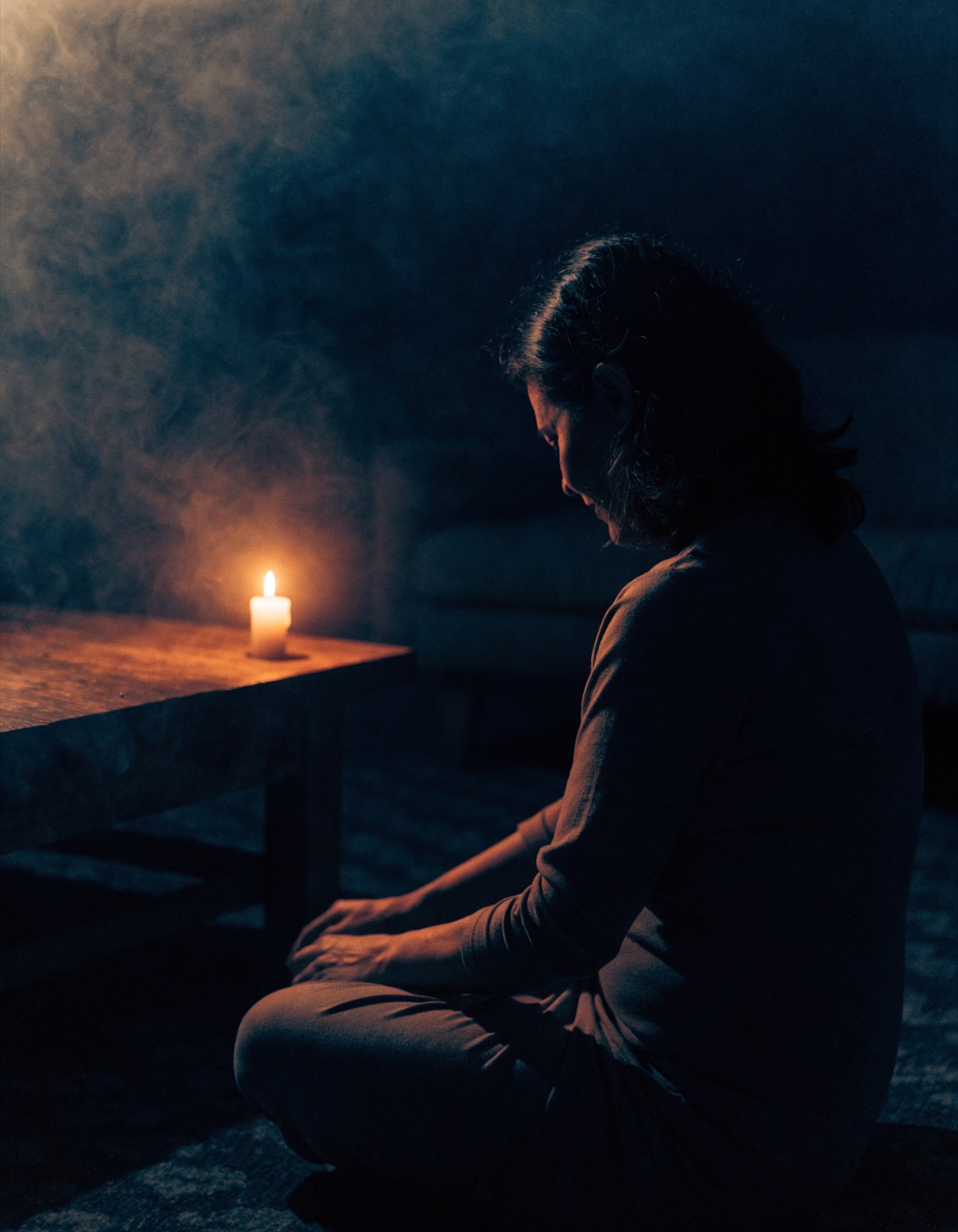 Mulher sentada no chão de uma sala escura, à luz de uma vela